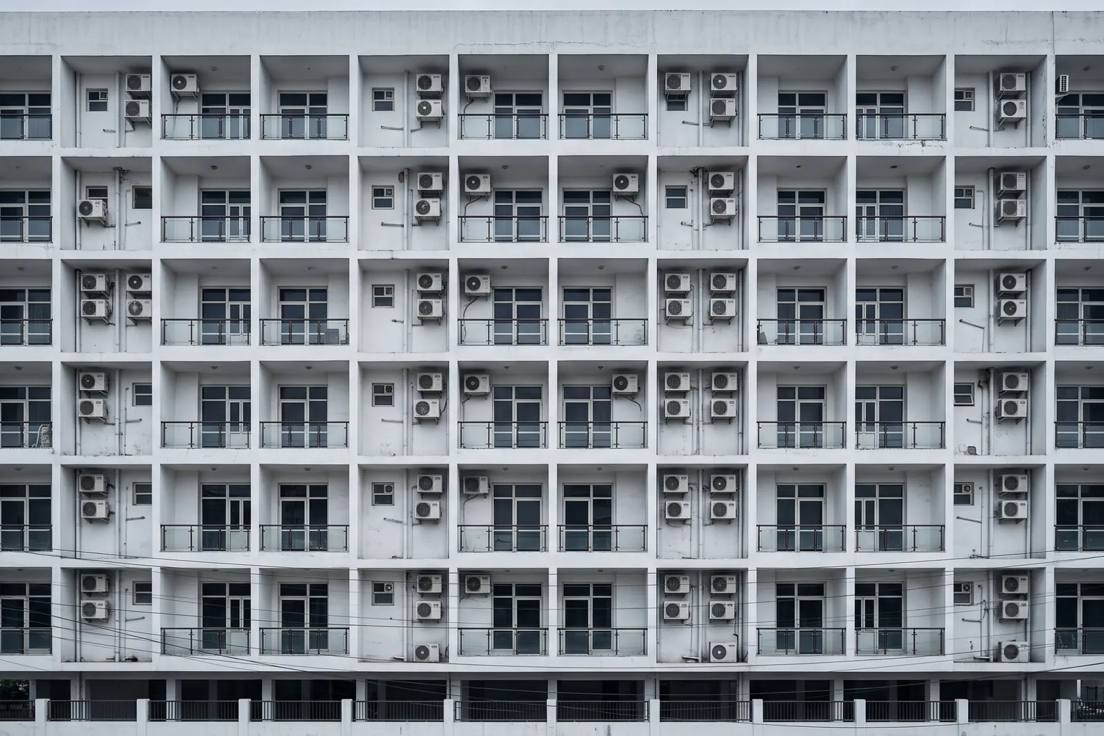 A white apartment facade with a strict grid of balconies and air conditioners