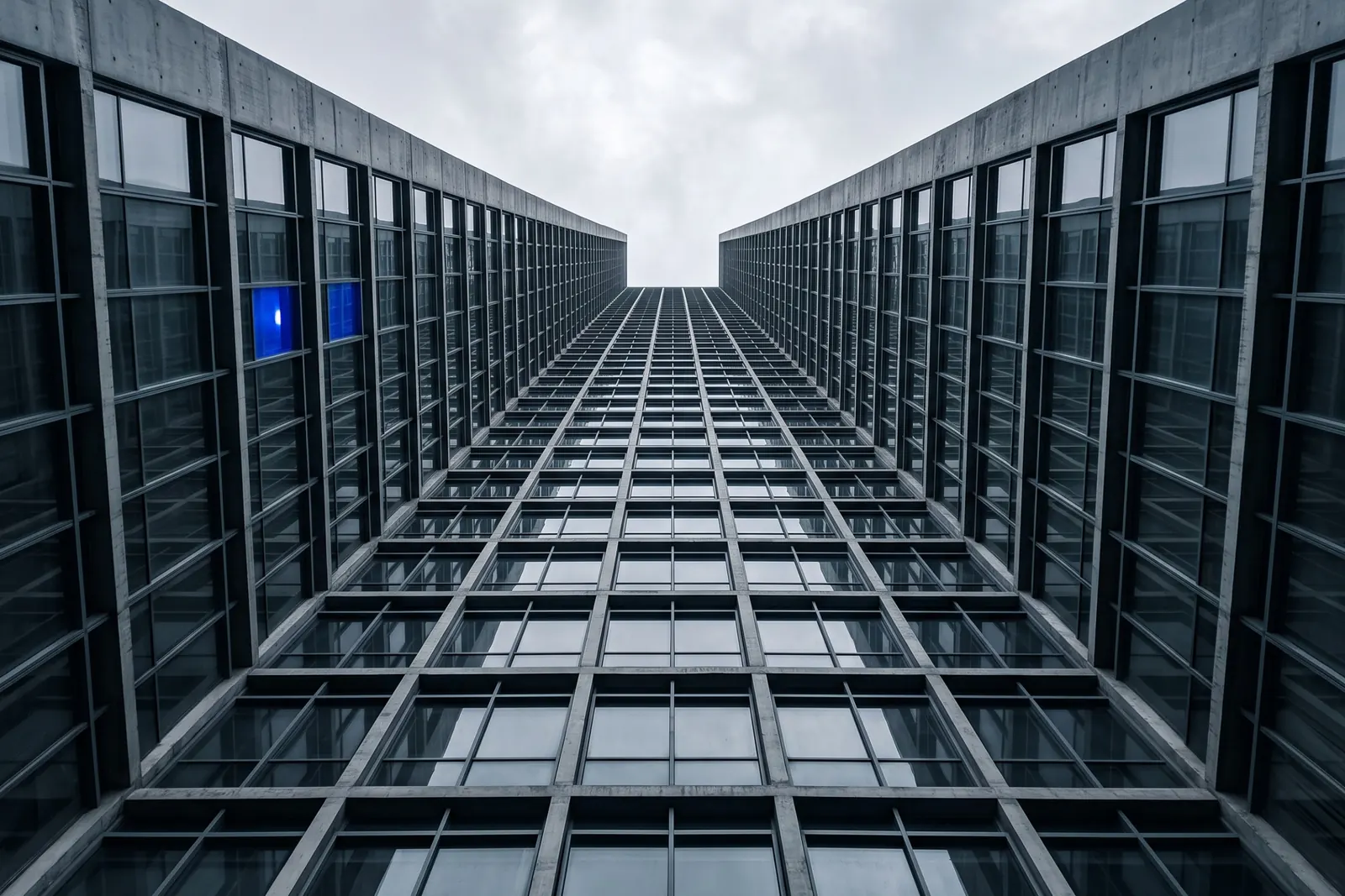 Looking up between two office tower facades, one window lit blue